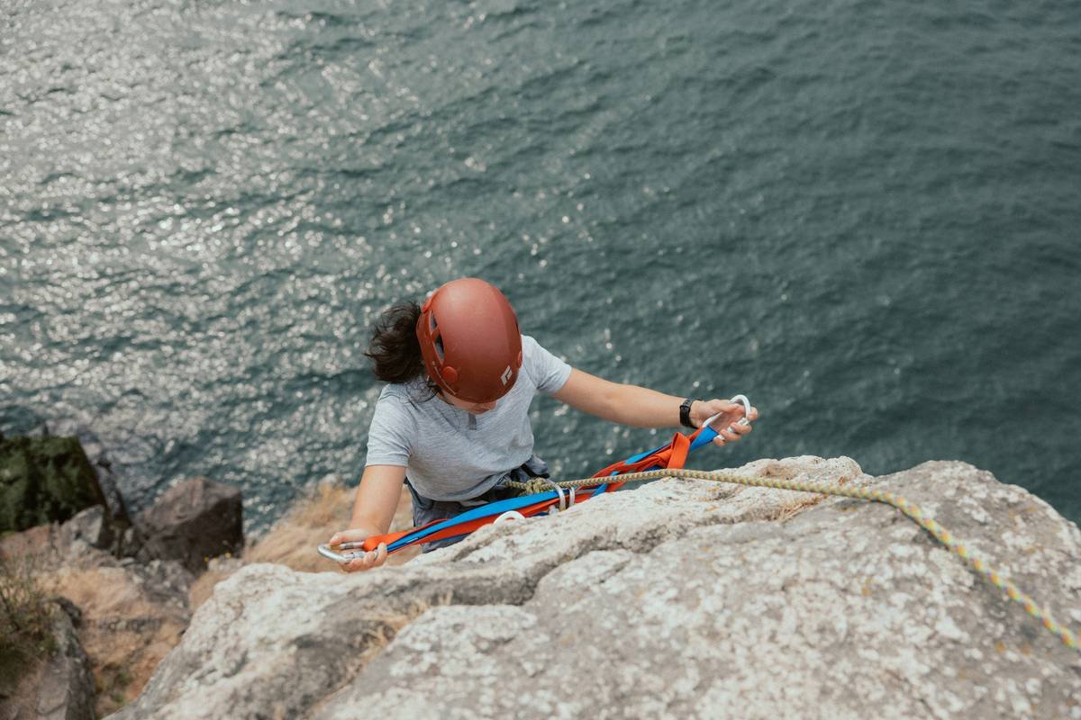 Climber evaluating a chockstone anchor in a sandstone crack, with rope threaded through and hand testing stability